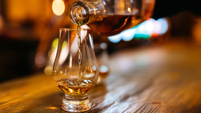 A person pouring a drink of whiskey into a Glencairn glass on a wooden counter