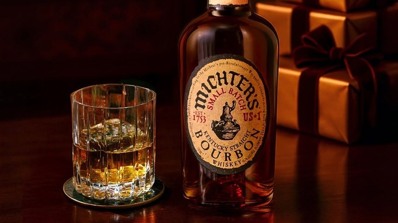A bottle of Michter's US*1 Bourbon on a wooden table next to a filled glass
