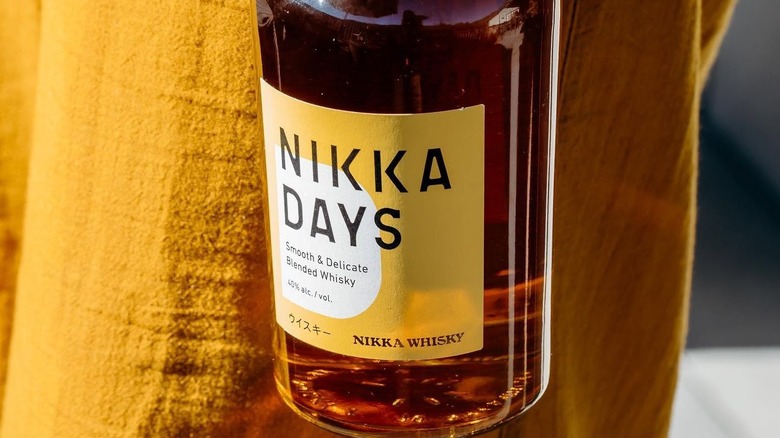 A close up shot of a person carrying a bottle of Nikka Days by their side