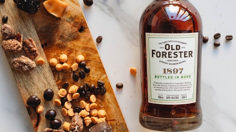 A bottle of Old Forester 1897 laid next to food that represents some of its tasting notes