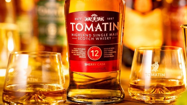 A close up of a bottle of Tomatin 12-year Sherry Cask with glasses either side