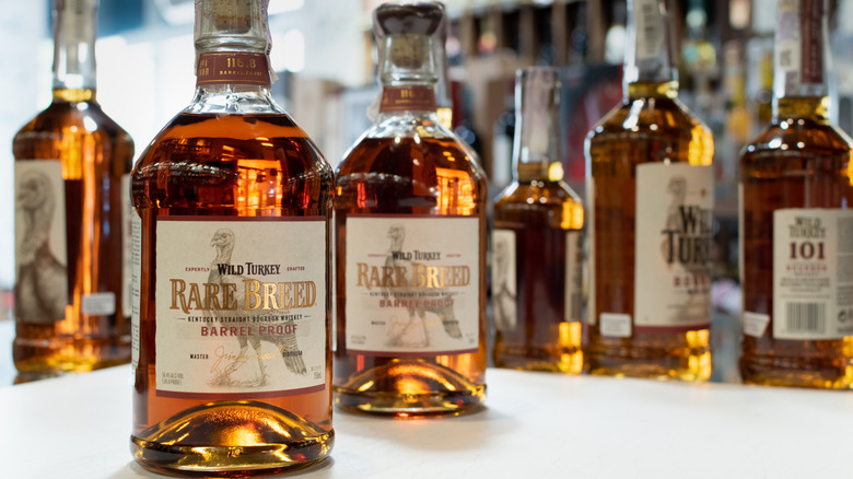 Two bottles of Wild Turkey Rare Breed placed on a white table with blurred bottles in the background