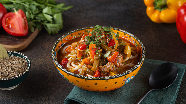 a colorful bowl of lagman served on a dark table