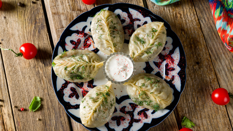 five manti served on a plate with sour cream