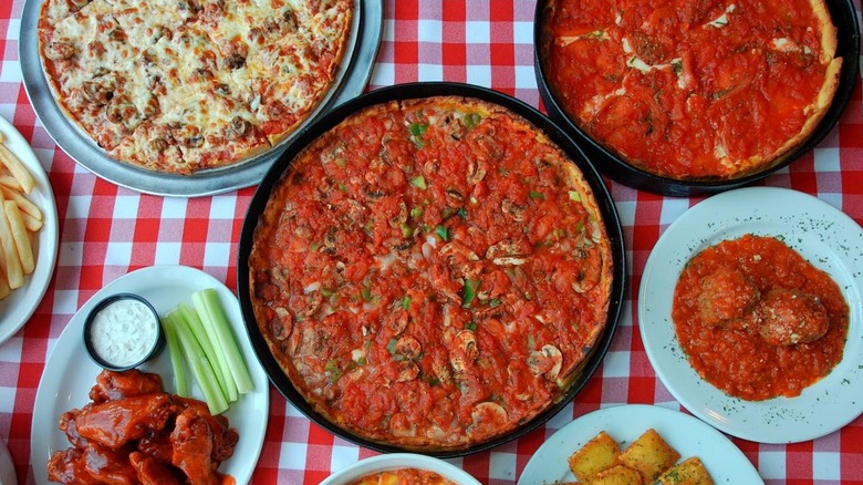Several dfferent pizzas with meatballs and wings on red and white checked tablecloth