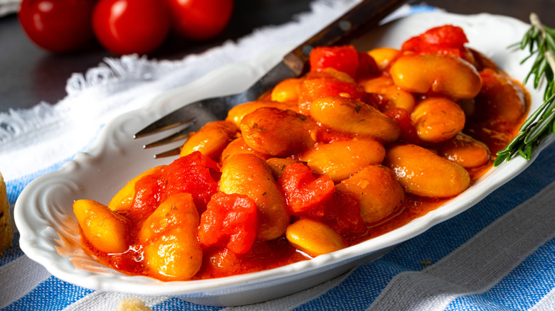 A white dish of Gigantes plaki set on a blue and white tablecloth.
