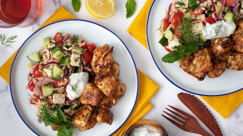 Chicken souvlaki and orzo salad on plates with tzatziki and fresh herbs