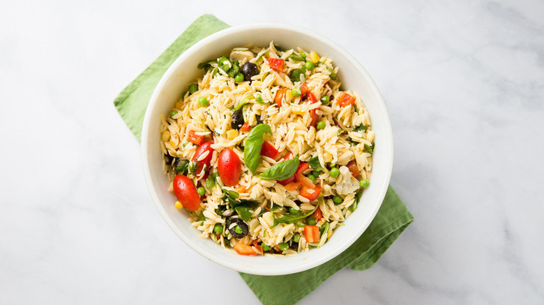 Orzo salad in white bowl with green linen underneath