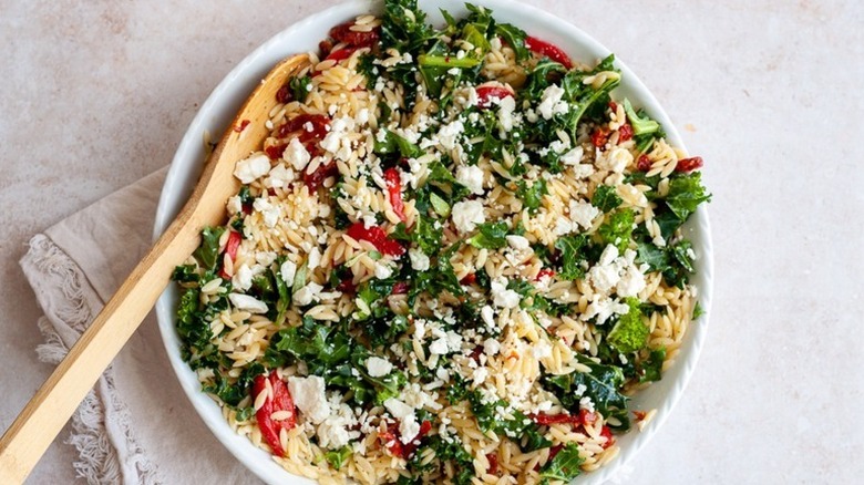 Bowl of orzo salad with wooden spoon