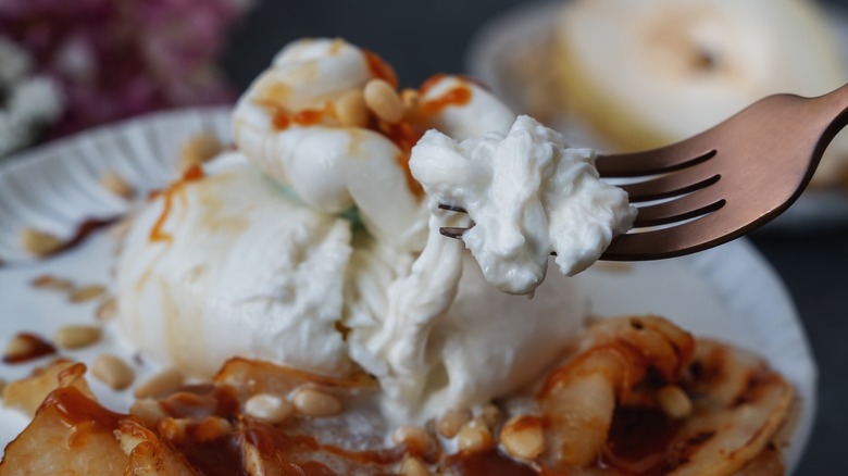 Fork lifting stracciatella from burrata ball, plated with marinated pear, pine nuts, and caramel sauce