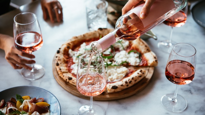 Hand pouring rose into glasses by burrata pizza