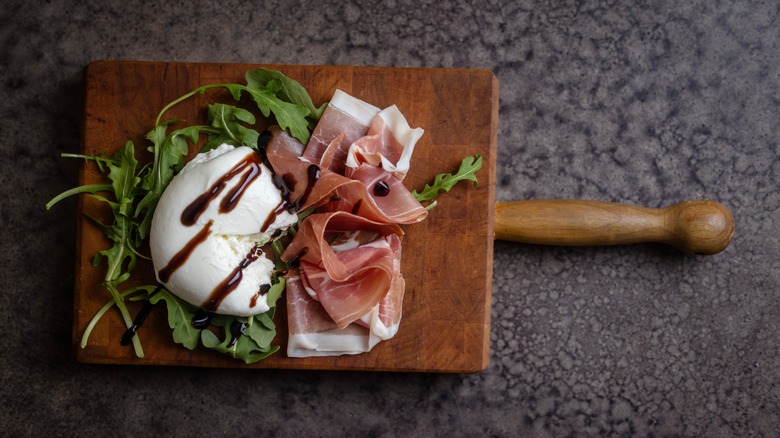 Burrata on wooden serving platter with prosciutto, arugula, and balsamic vinegar