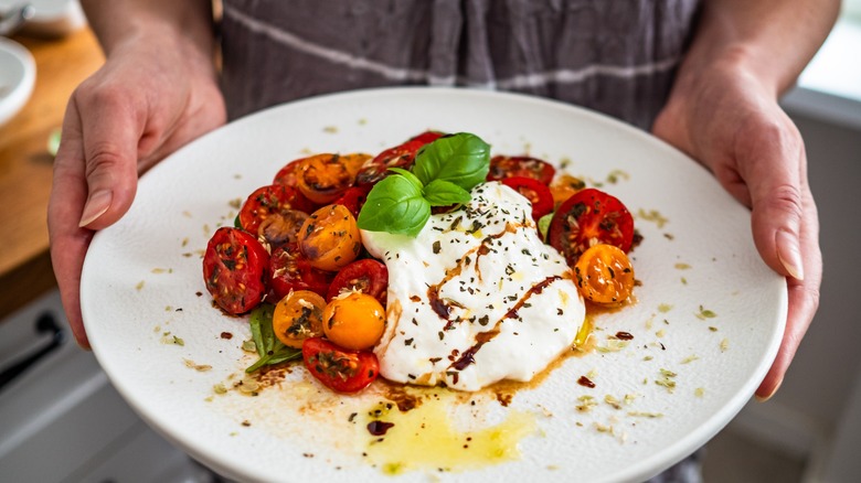 Hands holding tomato and basil salad with burrata