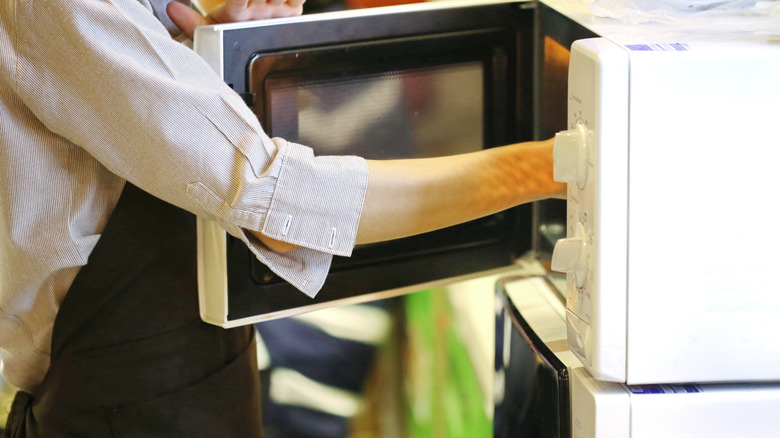 Person with apron with hand inside of microwave stacked on another microwave
