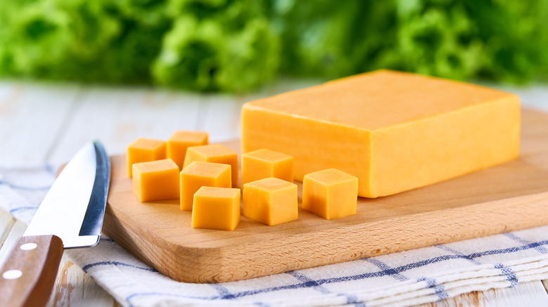 Block of cheddar with some cut into cubes on a cutting board