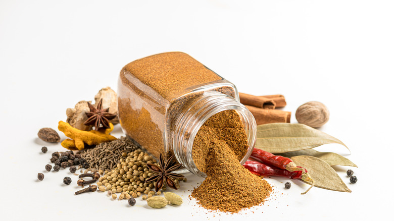 Garam masala spilling out of bottle, surrounded by the ingredients