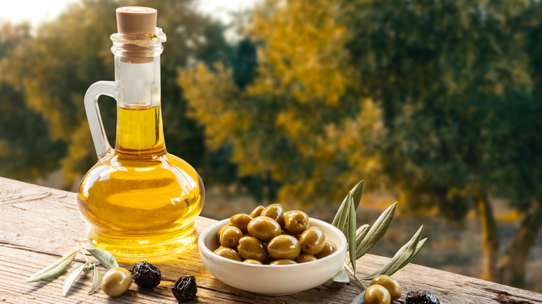 Olive oil in a pouring bottle, with a bowl of olives beside it