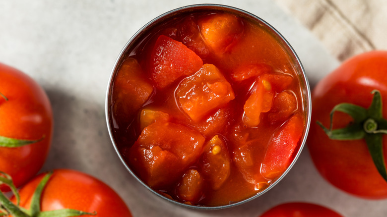 Open can of tomatoes with fresh tomatoes surrounding it