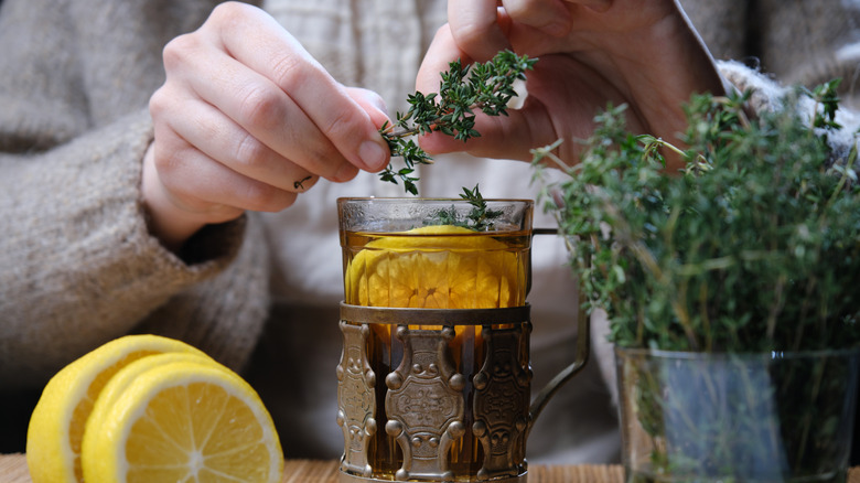 Person places a sprig of thyme in a cup of lemon tea