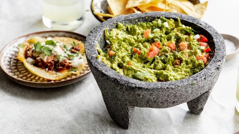 Guacamole in a mortar alongside tortilla chips and Mexican food