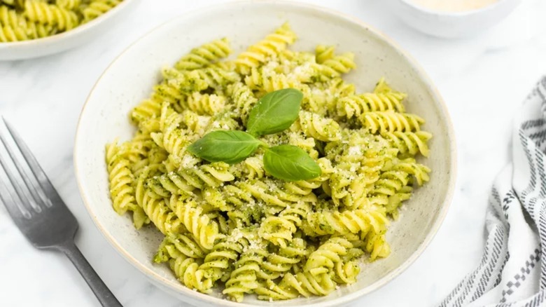 Basil pesto pasta in a bowl on a table with basil leaves on top