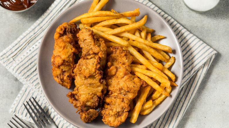 A plate of Idaho finger steaks with fries on a striped towel on a gray counter with forks and sauces partially in view