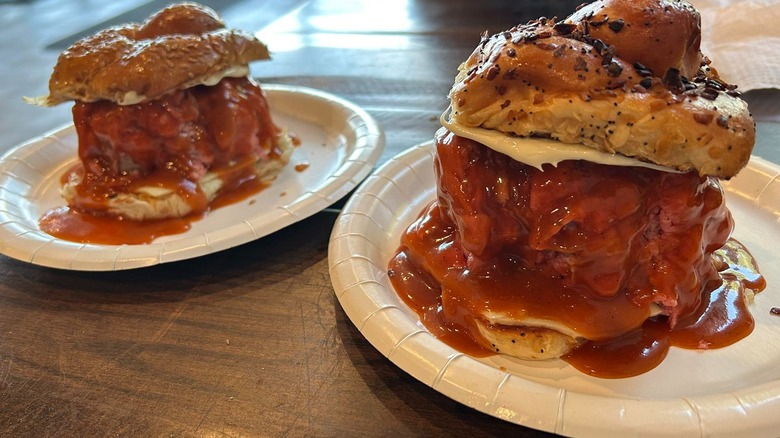 Two paper plates each with a roast beef sandwich dripping barbecue sauce on a wooden table