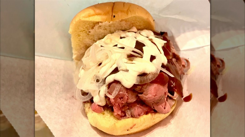 Pit beef sandwich topped with onions, horseradish, and barbecue sauce against paper, with mirror border