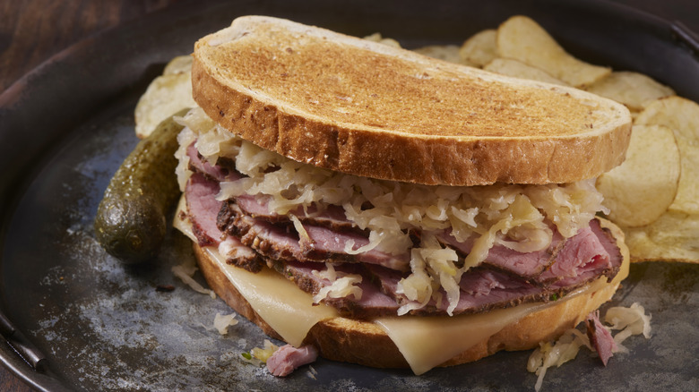 A Reuben sandwich with a pickle and chips on a dark plate with a wood background