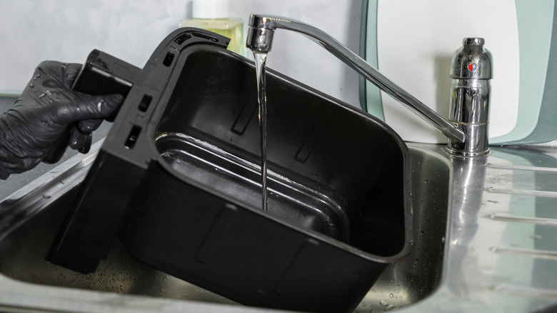 Hand with black glove holding an air fryer basket that they're washing in the sink