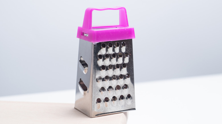 Cheese grater with bright pink handle on the edge of a white countertop