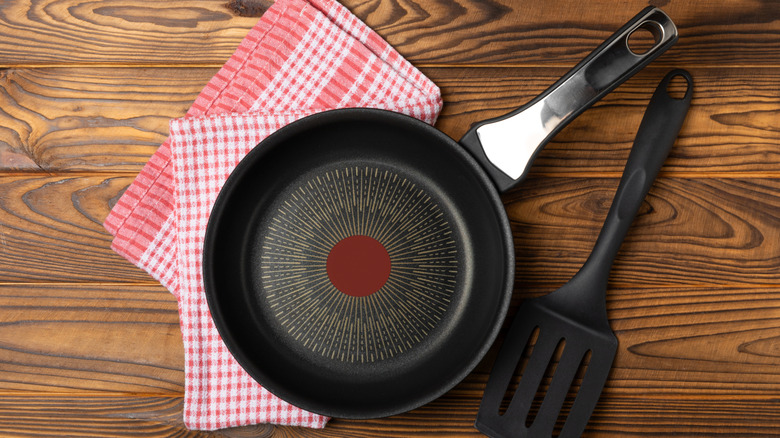 Nonstick pan on table with red checkered dishcloth and spatula