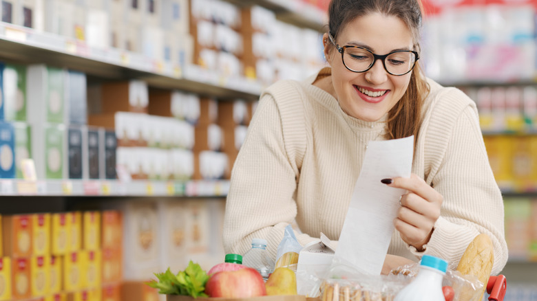 Woman happily looking at grocery store receipt while pushing shopping cart