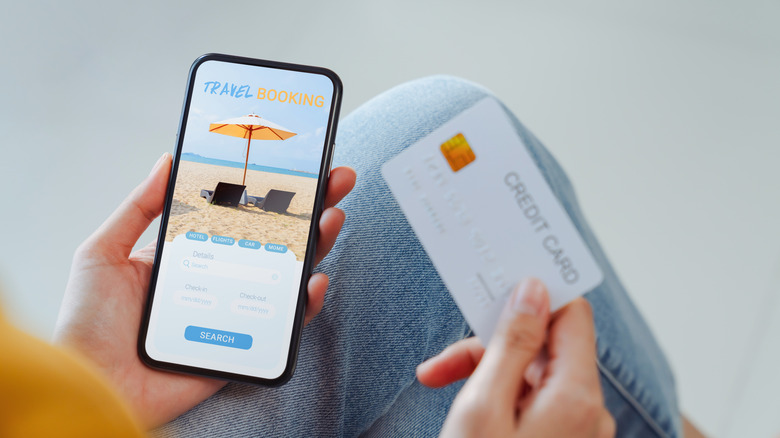 Woman holding her credit card and phone with a travel booking page open