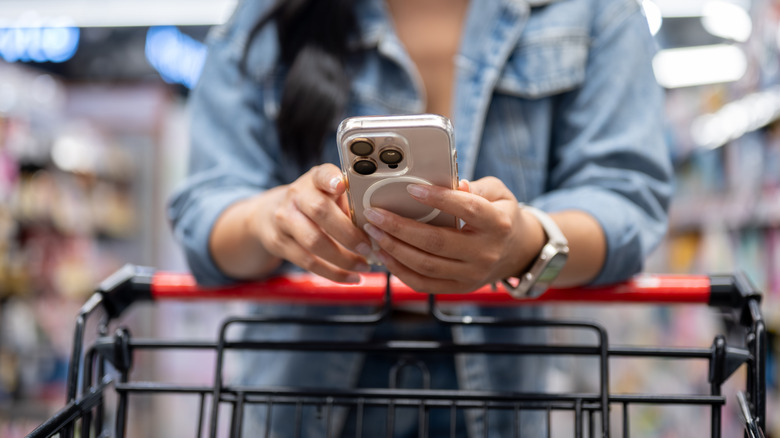 Woman using smart phone while pushing a shopping cart at a store