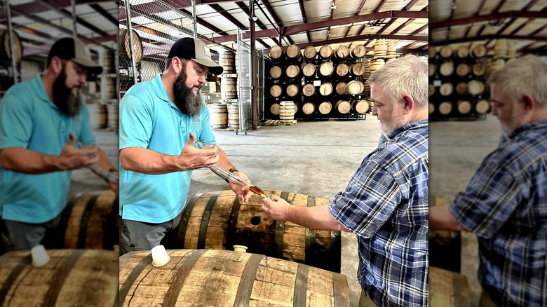 Distiller in a teal shirt dispensing bourbon directly from the barrel to a male patron in a plaid shirt.