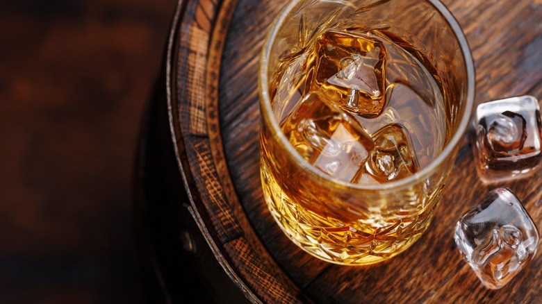Glass of whiskey on ice sitting on top of an aged barrel.