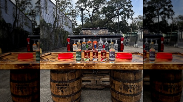 A tailgate-style makeshift bar set up on whiskey barrels with several bottles of spirits lining the bartop.