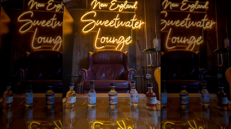 Vintage leather armchair in front of a neon sign reading New England Sweetwater Lounge, several nips line the table in the foreground.