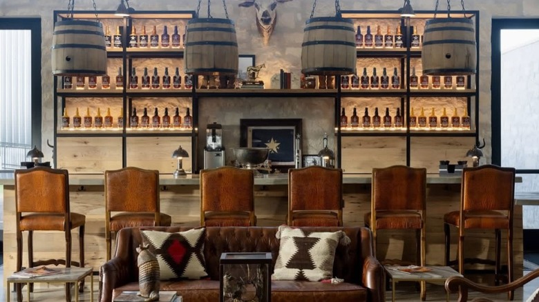 Upscale rustic whiskey bar with hanging lights fashioned from whiskey barrels and shelves of bourbon bottles.