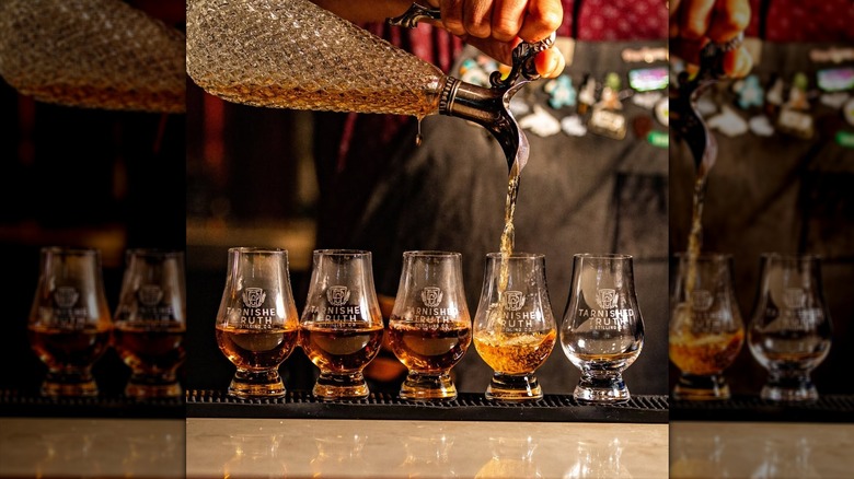 A crystal whiskey decanter pours bourbon into glasses on a black rubber bar mat.