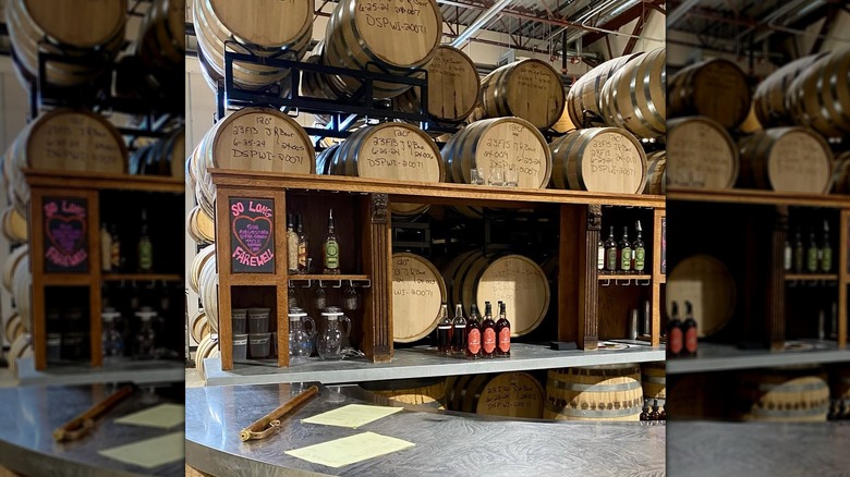 Stacked whiskey barrels behind a bar with hand-written distilling notes on the barrels' tops.