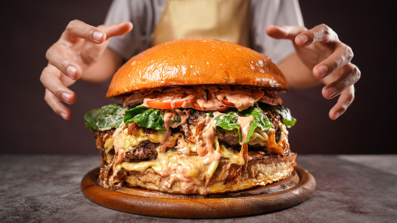 Hands reaching for a giant burger on a wooden tray