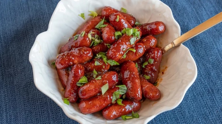 Bowl of spicy little smokies and a serving spoon topped with fresh herbs