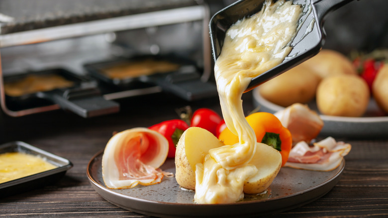 Melted raclette pouring over a plate of meats and vegetables