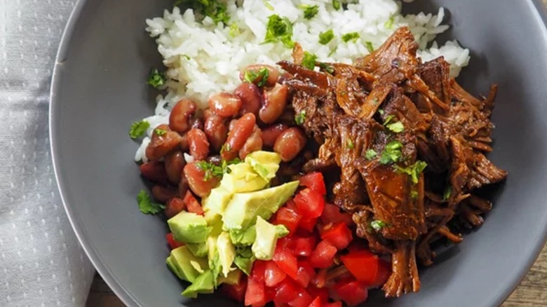 A bowl of Chipotle copycat barbacoa alongside rice, beans, tomatoes, and avocado topped with cilantro
