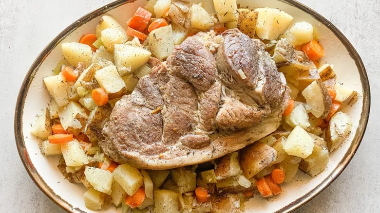 Pork roast in the middle of a platter, surrounded by potatoes and carrots