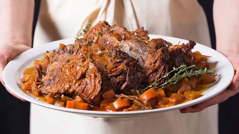 Woman holding plate of pot roast surrounded by carrots and thyme