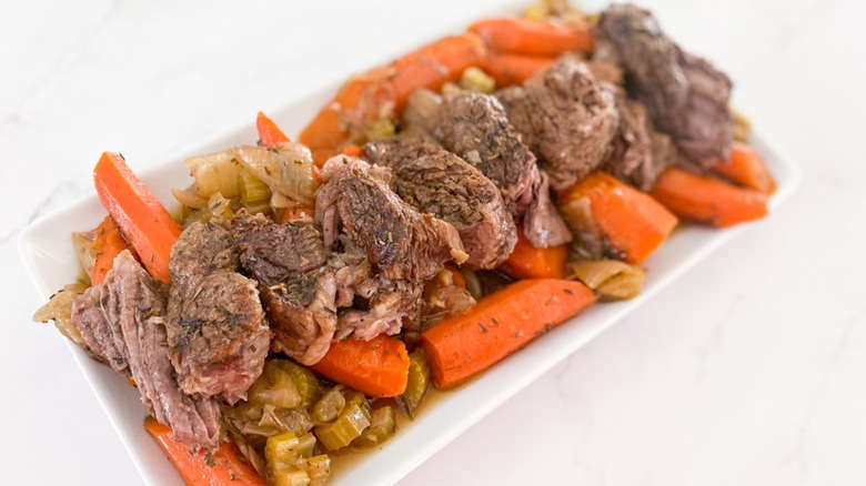 Platter of roast beef chunks on top of a celery, carrots, and onions