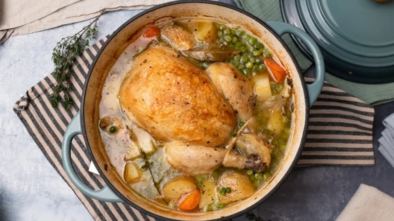 Roast chicken with carrots, potatoes, and peas in a blue enamel Dutch oven